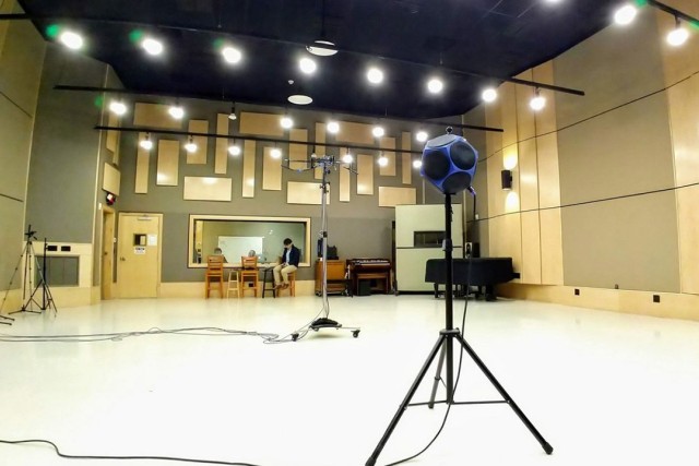 a large, mostly empty room with a multifaced speaker on a stand and another stand with microphones.