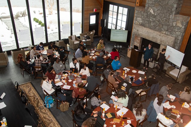 Over head picture of graduate school workshop. Students at tables with work supplies.