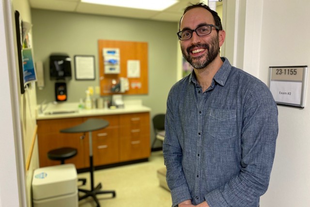 Man smiling, stands in front of a healthcare exam room.