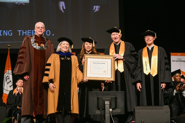 five people wearing graduation regalia holding an honorary degree in a frame.