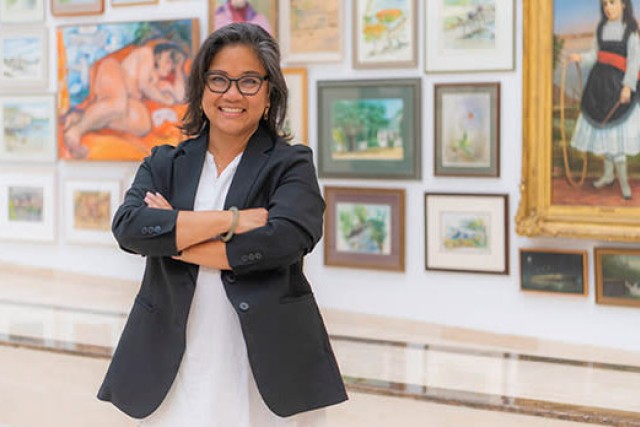 art gallery director standing with her arms crossed in front of a wall of paintings.