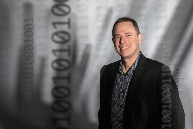 Evan Selinger appears in front of a gray backdrop wearing a black and gray suit.