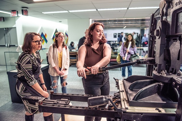 a woman looks on as another pulls a print on the Kelmscott/Goudy printing press in the Cary Library.
