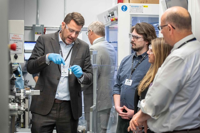 a man demonstrates battery useage to three bystanders in a research lab.