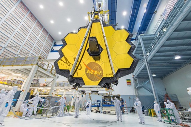 A groupf of NASA technicians lift the Webb Telescope using a crane to move it inside a clean room at NASA's Goddard Space Flight Center.