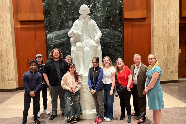a group of people stand in front of a marble statue.