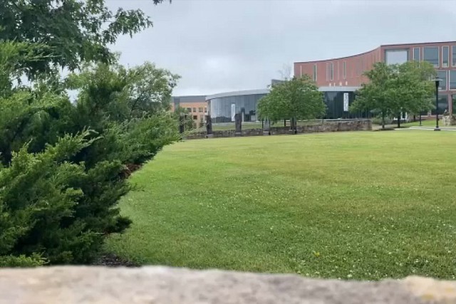 A photo of RIT campus showing the University Services Center in the distance. The foreground is mostly green lawn space in front of the building.