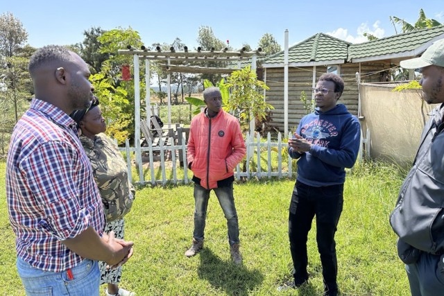 Five black men stand in a semicircle in a small garden in Kenya.