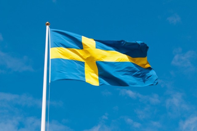 The blue and yellow flag of Sweden appears in a blue sky.