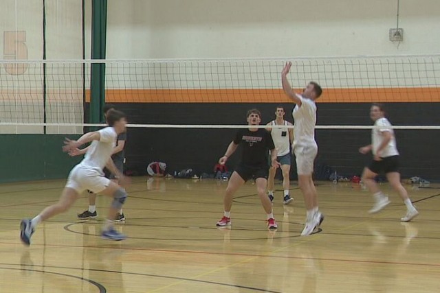 a group of men are shown playing a game of volleyball in a gymnasium.