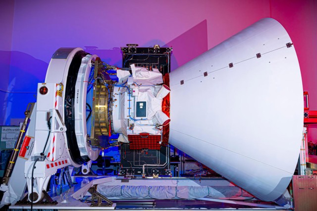 NASA's SPHEREx space telescope in a cleanroom, partially enclosed in a rocket payload fairing, with intricate wiring and thermal insulation visible under blue and red lighting.