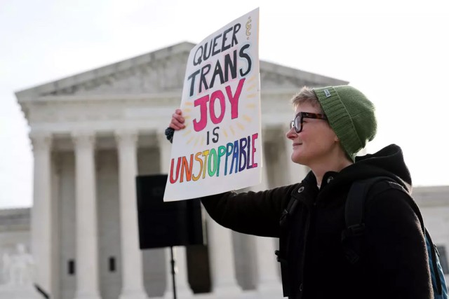 A transgender rights supporter holds up a protest sign that reads, queer and trans joy is unstoppable, outside of the Supreme Court building in Washington, D.C.