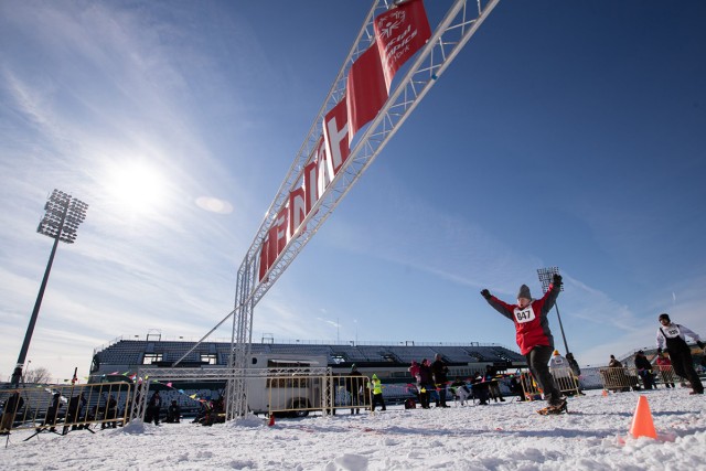 A snowshoer raises their arms in triumph as they cross the finish line.