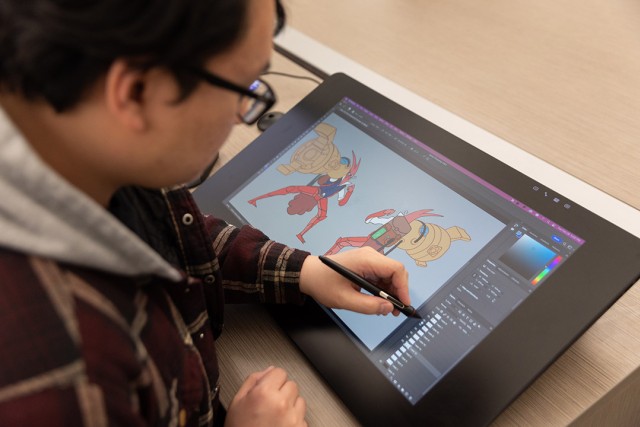 Person uses a stylus on a digital drawing tablet to illustrate cartoon robots.