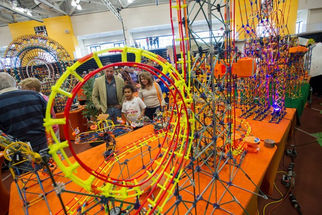 a family looks at a rollercoaster built with knex in a gymnasium setting.