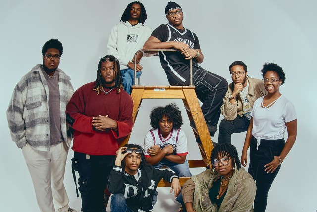 a group of men and women gather around a wooden step ladder and stand for a photo at different heights.