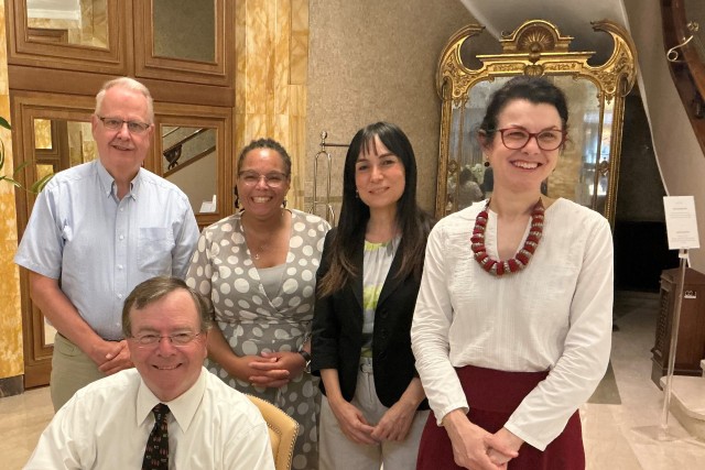 A group of people stand behind Gerry Buckley as he signs paperwork on a desk. They are all smiling. 