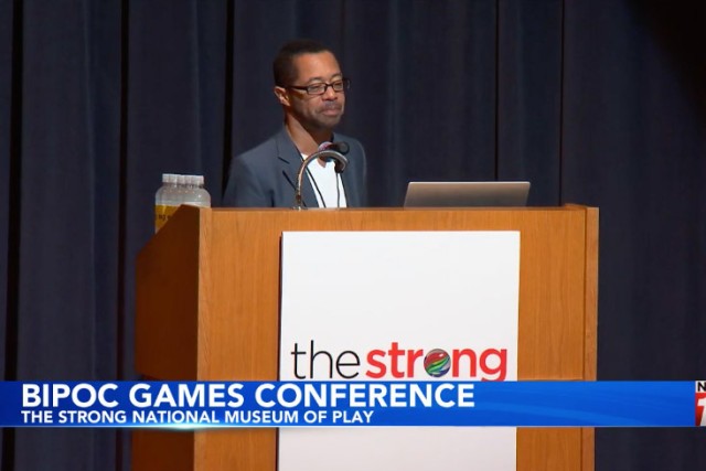 a man stands on a stage at a podium with the strong's logo displayed on the front.