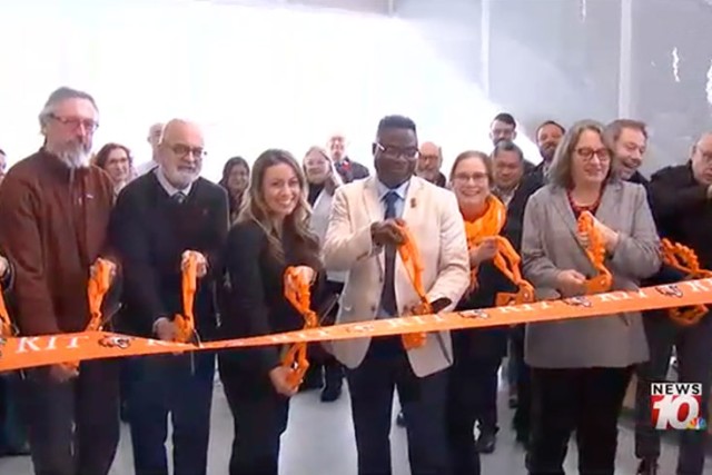several adults cut an orange R I T ribbon with large scissors.