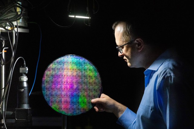 a man in profile holds a quantum photonic wafer against a black background.