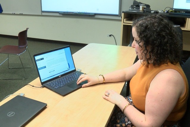 a woman works on an open laptop in a classroom.