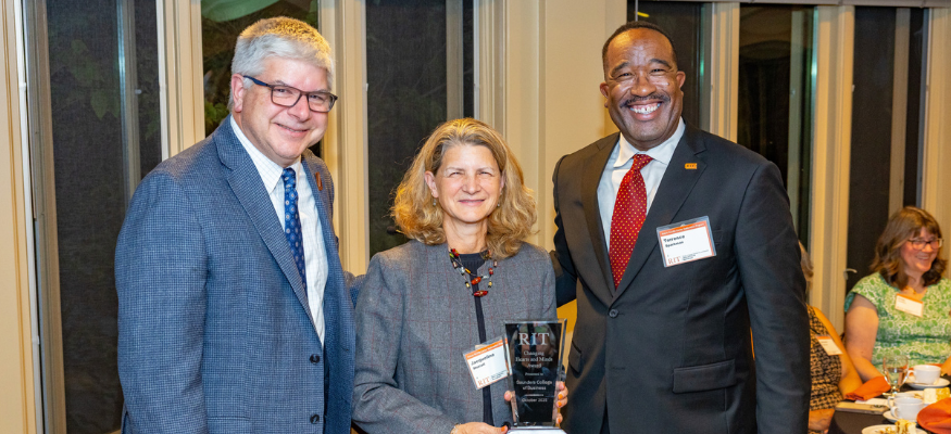 Group of three people, the middle woman is holding an award