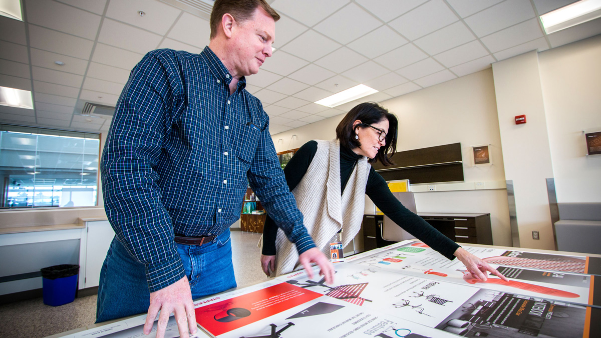 A man and woman looking over large printouts of different parts of office chairs