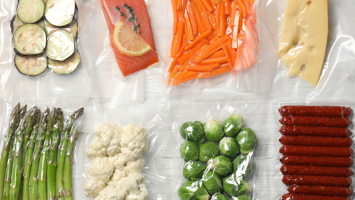Different food products in vacuum packs on white wooden table, flat lay