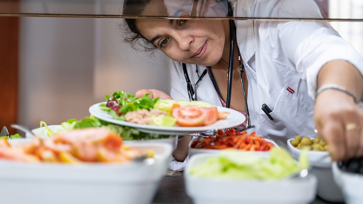A medical professional adding salad toppings to their plate at a salad bar.