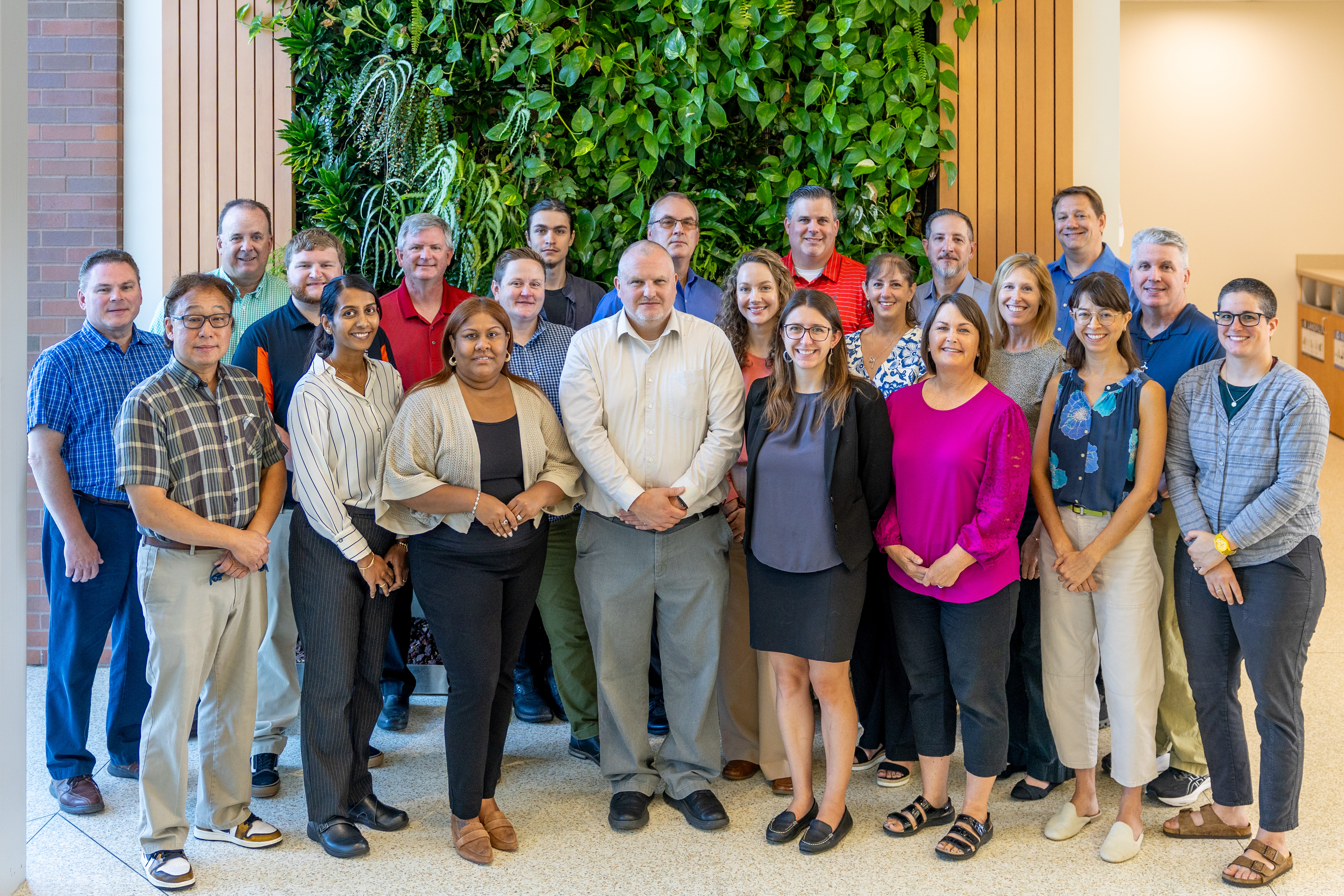NYSP2I group photo of staff in front of green plant wall