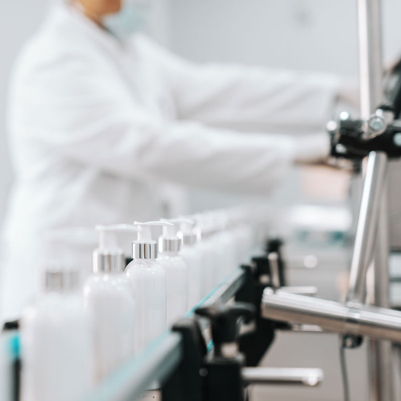Picture of bottles with hair conditioner in row on exit of pouring machine. Chemical factory interior. In background chemist.