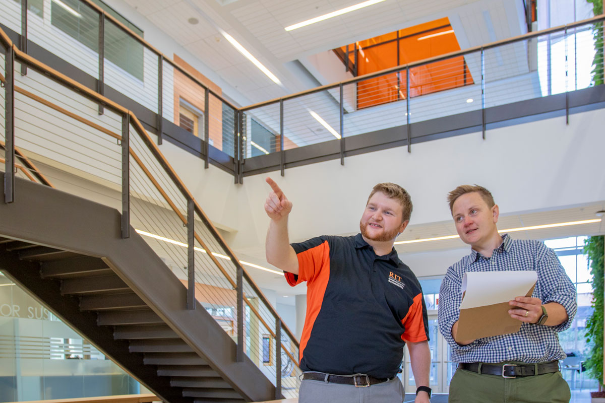 two people in the lobby area of the GIS building, one pointing and one with a clipboard
