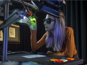 A student wearing sunglasses looks at something under a green light.