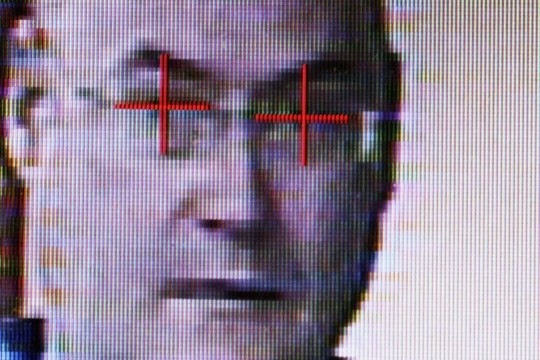 digitized image of man's face with red plus signs over the eyes.
