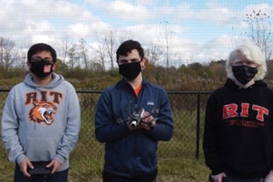 three students standing outdoors with a drone.