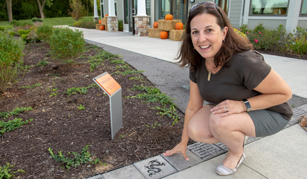 Woman posing with personalized paver at Lobozzo Alumni House