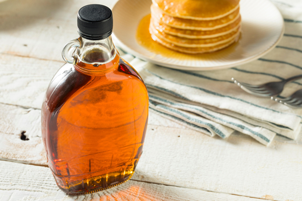 Maple syrup and pancakes on table