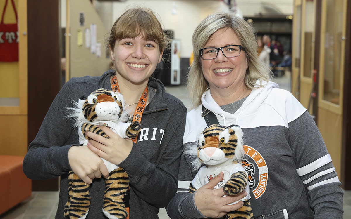 Two women holding Ritchie, the mascot plushie