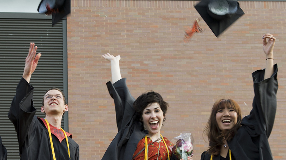 A group of graduates in their gowns, tossing their caps into the air.