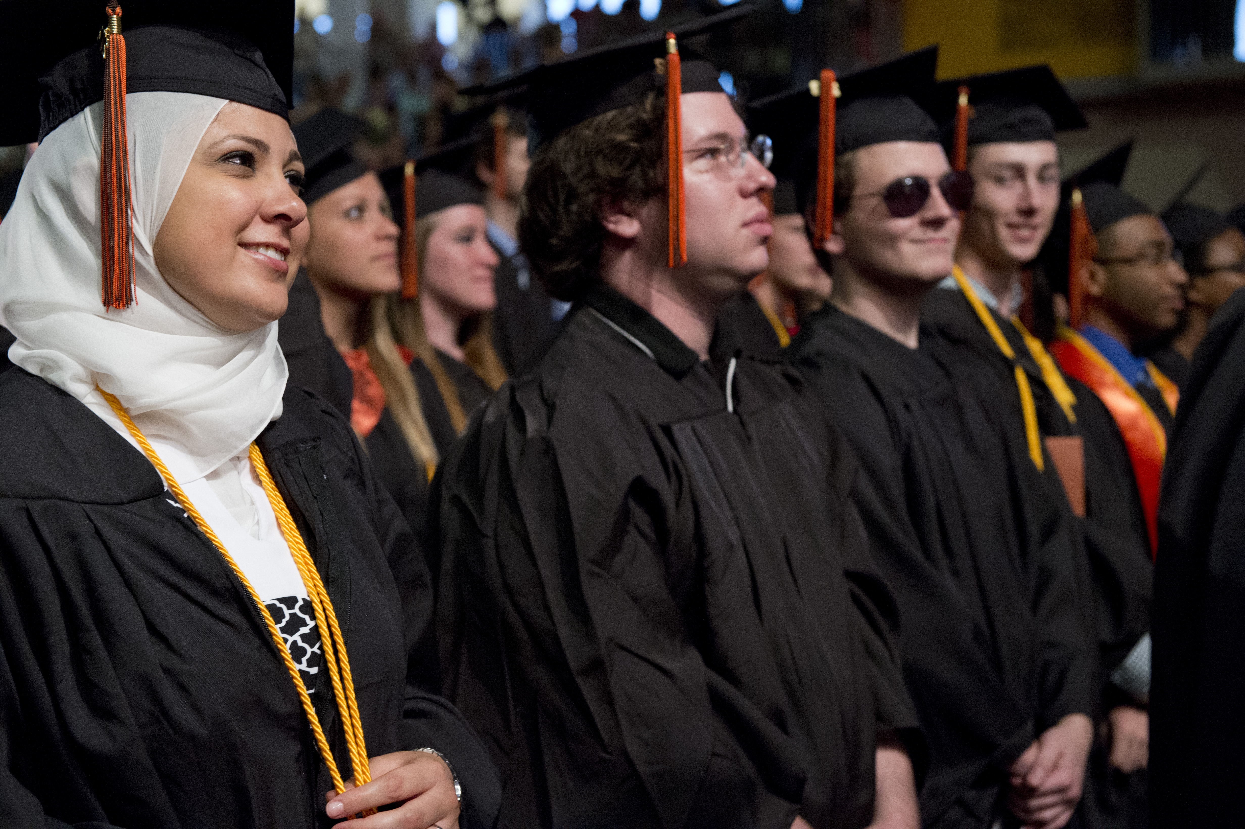 students standing at commencement in cap and gown while looking toward stage