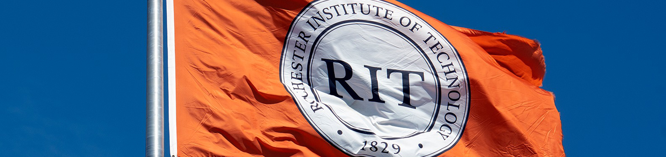 orange flag flying in the wind with an RIT logo in the middle