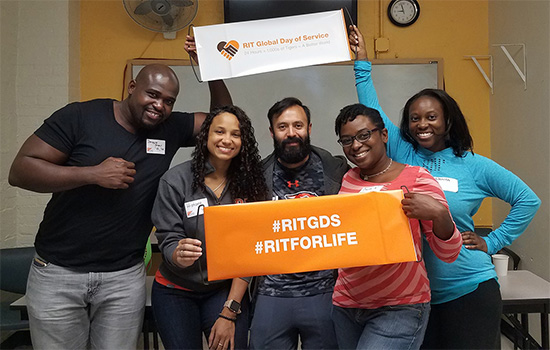 RIT alumni holding an orange sign with the text #RITforLife