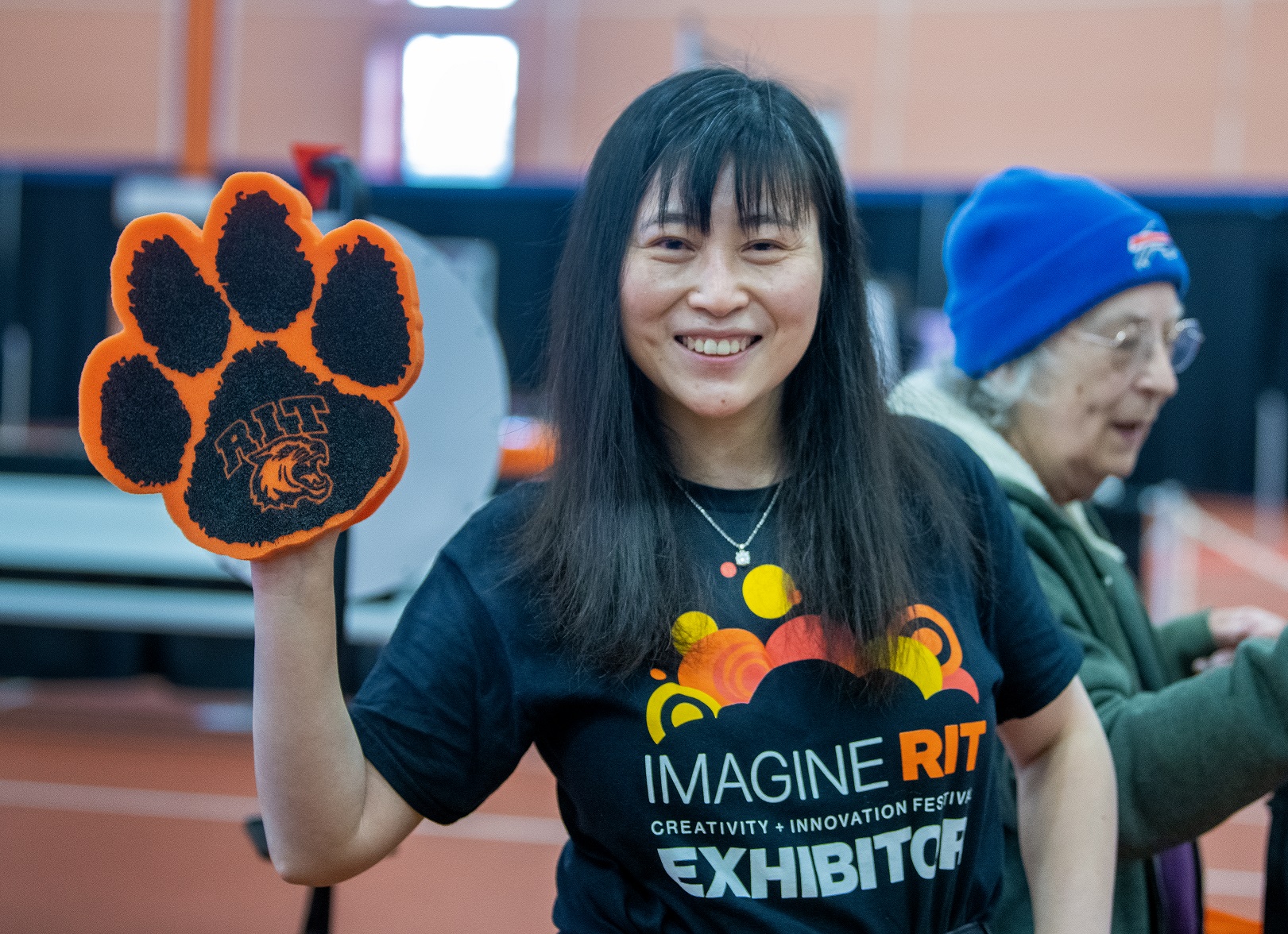 a photo of a person wearing an Imagine RIT t-shirt and holding up a foam paw