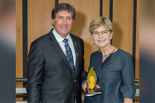 Steve Wear and Sophia Maggelakis pose for a photo together, Wear holding the distinguished alumni award trophy.