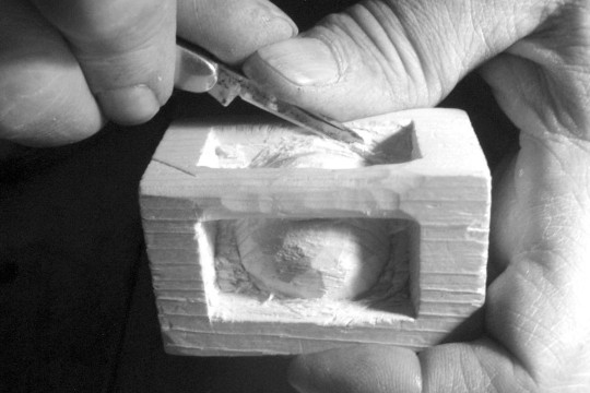 hands carving a ball into a small block of wood.