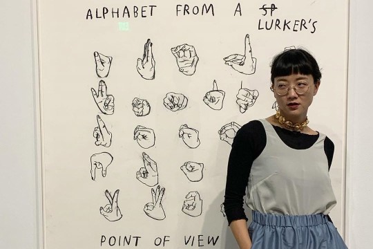 woman standing next to charcoal drawing of American Sign Language alphabet.