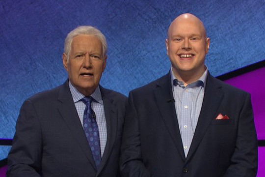 Alex Trebek standing with Jeopardy contestant.