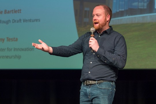 man holding microphone giving presentation on a stage.