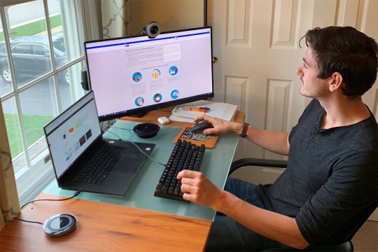 person sitting at home office desk working on laptop and computer monitor.