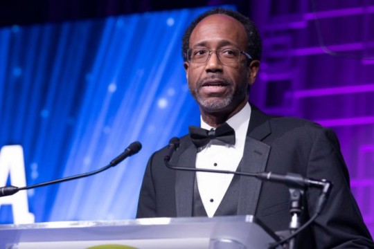 man in tuxedo speaking at podium.